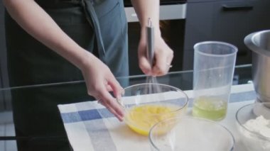 Profesyonel şef kek pişiriyor. Genç ve çekici ev hanımı şeker ve yumurtayı kaseye karıştırmak için çırpıyor, sonra da büyük metal kaseye döküyor.