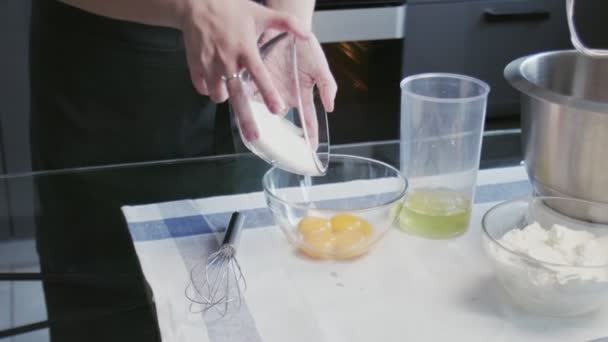 プロのシェフがケーキを作っています。若い魅力的な主婦はボウルに砂糖と卵を混ぜるために泡立て器を使用します — ストック動画