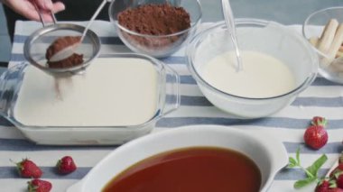 Profesyonel şef tiramisu keki pişiriyor. Genç ve çekici ev hanımı kakao tozuyla tiramisu kekinin tozunu alıyor.