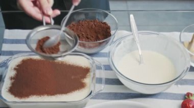 Profesyonel şef tiramisu keki pişiriyor. Genç ve çekici ev hanımı kakao tozuyla tiramisu kekinin tozunu alıyor.