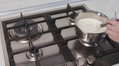 Profesyonel şef kek pişiriyor. Tanınamaz haldeki bir kadın tencerede acı krema sosu pişiriyor ve ocağın üstünde duruyor.