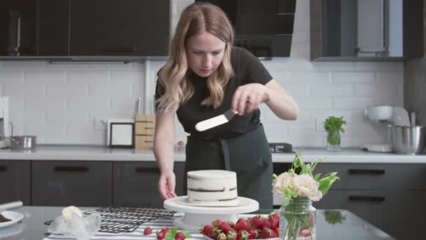 Profi-Koch kocht Kuchen. Junge attraktive Hausfrau richtet weiße Sahne mit Metallspachtel und Drehtisch auf Schokoladenkuchen aus — Stockvideo