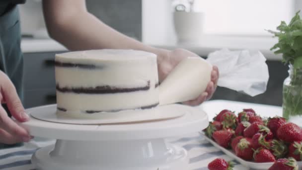 Chef profissional está cozinhando bolo. Jovem dona de casa atraente coloca creme branco no lado do bolo — Vídeo de Stock