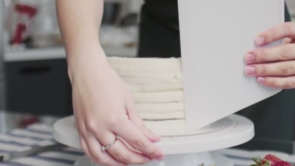 Chef profissional está cozinhando bolo. Jovem dona de casa atraente usa grande espátula de plástico e mesa rotativa para alinhar creme branco no bolo de chocolate — Vídeo de Stock
