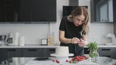 Profesyonel şef kek pişiriyor. Kadın, modern bir mutfakta güzel beyaz bir pastanın üstüne çilek koyar.