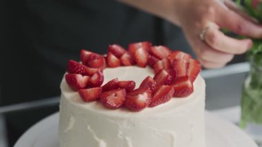 Profesyonel şef kek pişiriyor. Modern bir mutfakta güzel beyaz bir pastanın üstüne çilek koyan bir kadın.
