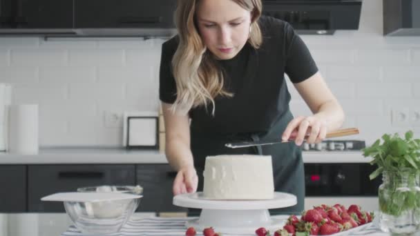 Professionell kock lagar tårta. Ung attraktiv hemmafru använder metall spatel justerar vit grädde på chokladkaka — Stockvideo