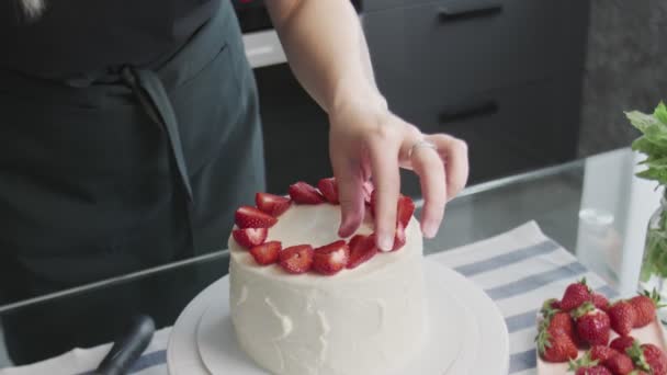 プロのシェフがケーキを作っています。最新のキッチンで美しい白いケーキの上にイチゴを置く女性のクローズアップ — ストック動画