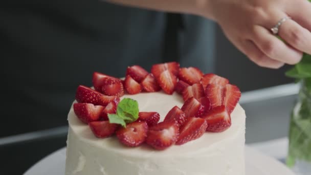El chef profesional está cocinando pastel. Primer plano de la mujer coloca fresa en la parte superior de un hermoso pastel blanco en una cocina moderna — Vídeo de stock