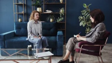 Genç kadın modern çatı katı tarzı stüdyoda koltukta oturan psikologla konuşuyor. Psikolog onu dinler ve hasta sorunlarını anlatırken yazar..