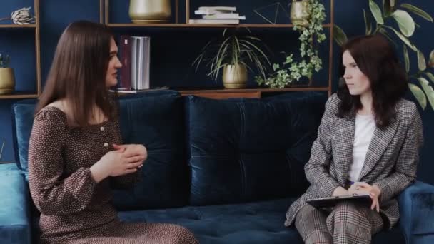 Расстроенная молодая женщина, сидящая на диване и разговаривающая с психологом на сеансе терапии — стоковое видео