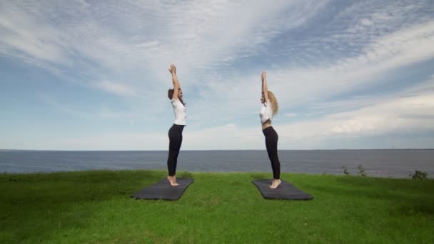 Dos mujeres jóvenes practicando meditación y yoga en la naturaleza en el acantilado de alta montaña cerca del mar . — Vídeos de Stock