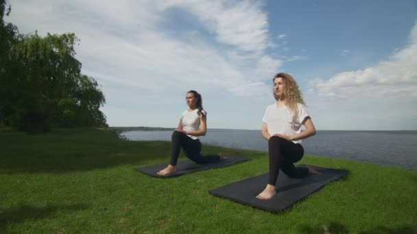 Due giovani donne praticano yoga sulla costa vicino al lago o al mare. Formazione Crescent Lunge sulla posa del ginocchio . — Video Stock