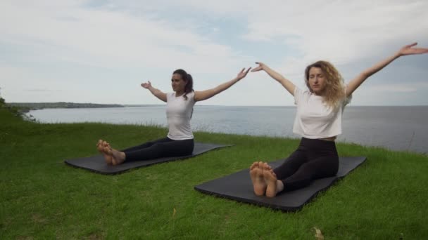 Due giovani donne praticano yoga sulla costa vicino al lago o al mare. Formazione Personale Dandasana pose . — Video Stock