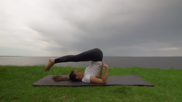 Young fit woman practice yoga on coast near the lake or sea. Woman doing Plow Halasana Pose — Stock Video