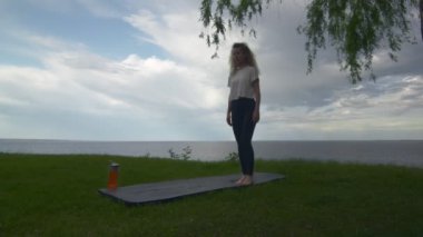 Genç ve formda bir kadının göl ya da denizin kıyısında yoga yapışının arkası. Yarım Lotus Kollu Kadın pozu.