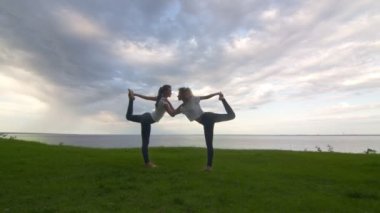 Aktif kıyafetli iki kadın kameraya poz veriyor ve yoga kralı pozu veriyor.