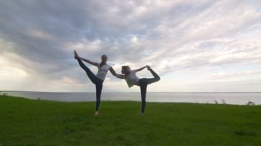 Aktif kıyafetli iki kadın kameraya poz veriyor ve birlikte yoga yapıyorlar Dansın Efendisi pozu ve Ayakta Ayakta Ayakta Parmak pozu veriyorlar.