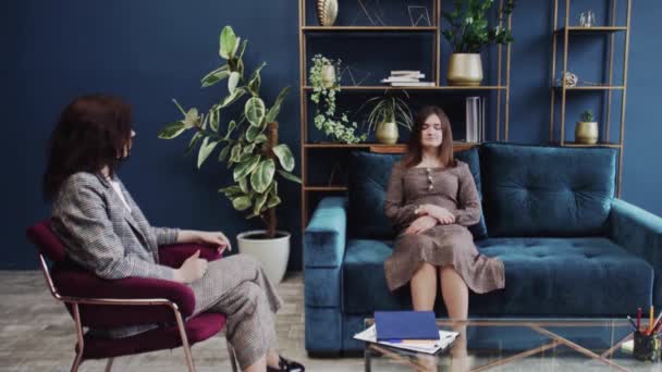 Young woman with closed eyes lying on sofa and listening psychologist at therapy session — Stock Video