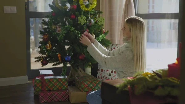 Snygg tjej i tröja dekorerar julgran med gula bollar. Vacker jul interiör. — Stockfoto
