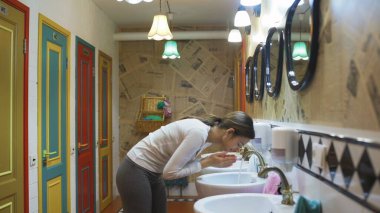 Genç güzel kadın otel umumi tuvaletinde yüzünü yıkıyor.