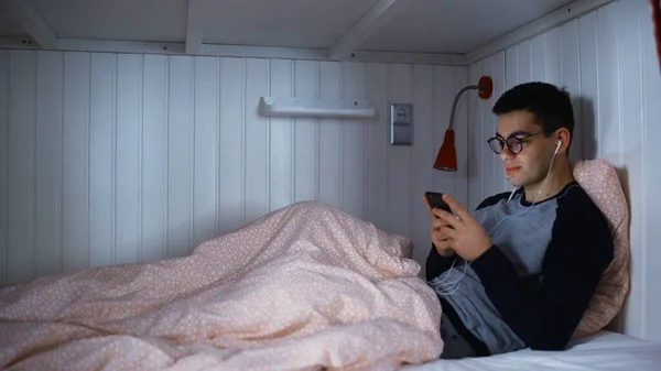 Mladý muž web surfování na svém mobilním telefonu na posteli v hostelu pokoj — Stock fotografie