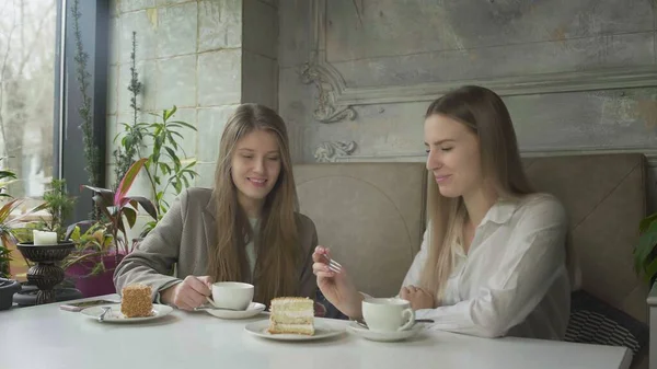 Δύο όμορφες νεαρές γυναίκες πίνουν καφέ και τρώνε κέικ στο καφέ. — Φωτογραφία Αρχείου