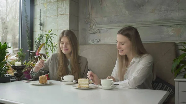 Две красивые девушки пьют кофе и едят торты в кафе — стоковое фото