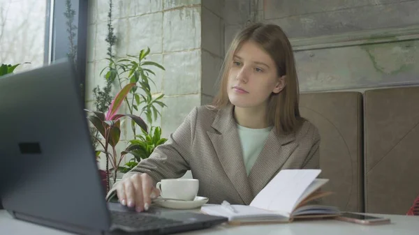 Beautiful young woman working with laptop in cafe and drinking coffee — Stock Photo, Image