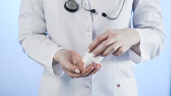Doktor nalévá bílé pilulky z láhve na modré pozadí — Stock fotografie
