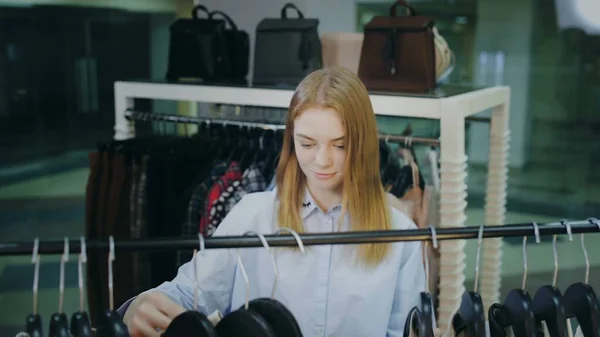 Attractive female customer looking on clothes on hangers in shop — Stock Photo, Image