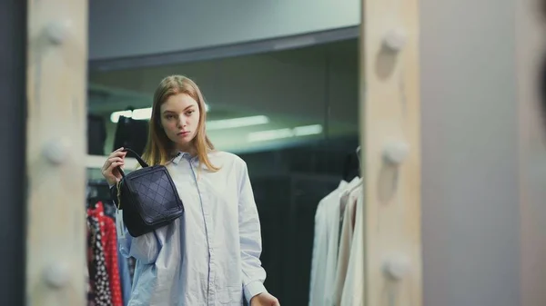 Attractive woman trying on handbags in front of a mirror in a boutique — Stock Photo, Image