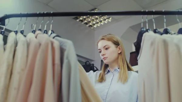 Female customer is viewing goods on rack in clothing store — Stock Photo, Image