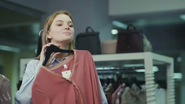 Attractive female customer looking at the mirror and trying on blouse in fitting room — Stock Photo, Image