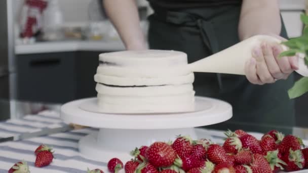 El chef profesional está cocinando pastel. Joven ama de casa atractiva pone crema blanca en el lado de la torta — Vídeos de Stock