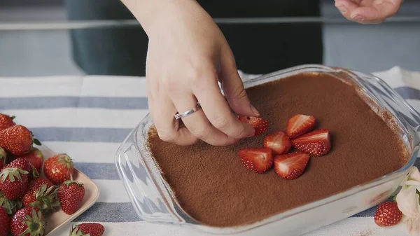 Ik kook thuis tiramisu cake. Close-up van de vrouw plaatsen aardbei op de top van een mooie tiramisu taart — Stockfoto