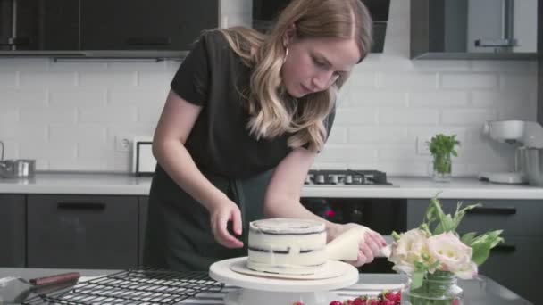 Le chef cuisinier cuisine des gâteaux. Jeune femme au foyer attrayante utilise spatule métallique et table tournante pour aligner la crème blanche sur gâteau au chocolat — Video