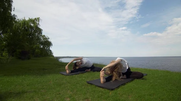 Duas mulheres meditando ao ar livre sentadas na borda da costa perto do mar, meia postura de lótus dedos dobrados gesto mudra fazer exercício de ioga de manhã. Duas mulheres praticando Revolved Head to Knee pose — Fotografia de Stock