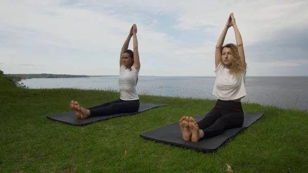 Duas mulheres jovens praticam ioga na costa perto do lago ou do mar. Treinamento Staff Dandasana pose . — Fotografia de Stock