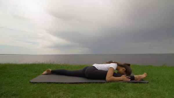 Jovem mulher apto praticar ioga na costa perto do lago ou do mar. Mulher sentada na frente Splits Hanumanasana pose — Fotografia de Stock
