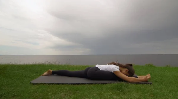 Jovem mulher apto praticar ioga na costa perto do lago ou do mar. Mulher sentada na frente Splits Hanumanasana pose — Fotografia de Stock