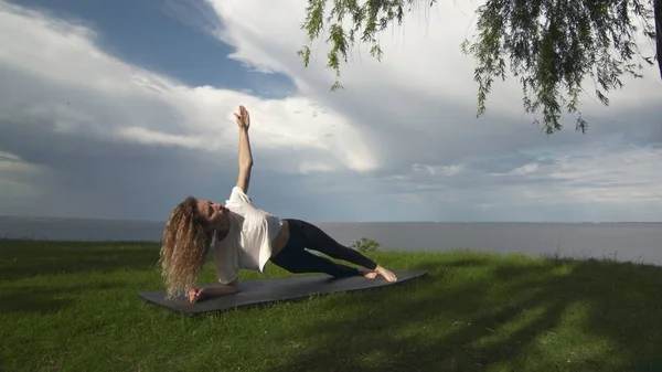 Jovem mulher apto praticar ioga na costa perto do lago ou do mar. Mulher fazendo lado antebraço prancha dose — Fotografia de Stock