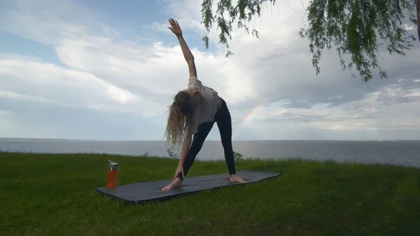 Jovem mulher apto praticar ioga na costa perto do lago ou do mar. Mulher fazendo Poses Triângulo — Fotografia de Stock