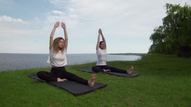 Dos mujeres meditando al aire libre sentadas en el borde de la costa cerca del mar, medio loto posan dedos doblados gesto mudra hacer ejercicio de yoga por la mañana. Dos mujeres practicando yoga posa — Vídeos de Stock