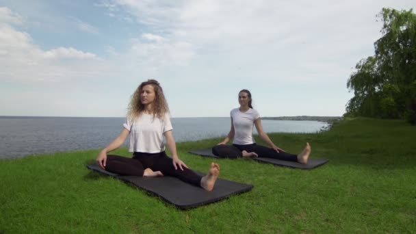 Due donne che meditano all'aperto seduti sul bordo della costa vicino al mare, mezzo loto posa dita piegate gesto mudra fare esercizio di yoga al mattino. Due donne che praticano Revolved Head to Knee posa — Video Stock