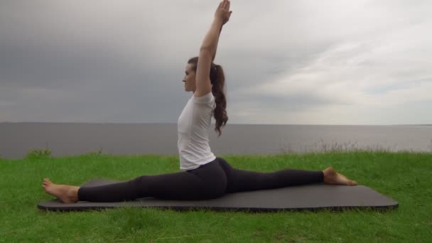 Mujer en forma joven practica yoga en la costa cerca del lago o el mar. Mujer sentada en Front Splits Hanumanasana pose — Vídeos de Stock
