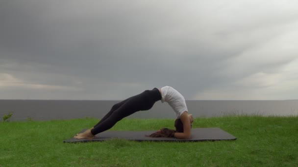 Młoda, sprawna kobieta ćwiczy jogę na wybrzeżu w pobliżu jeziora lub morza. Kobieta robi odwrócony personel Dvi Pada Viparita Dandasana pozować — Wideo stockowe