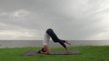 Genç, formda bir kadın göl ya da deniz kıyısında yoga yapıyor. Desteklenen Baş Duruş 3: Salamba Sirsasana C Pozu Yapan Kadın