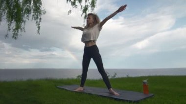 Genç, formda bir kadın göl ya da deniz kıyısında yoga yapıyor. Beş Noktalı Yıldız ve Üçgen Pozisyonları Yapan Kadın