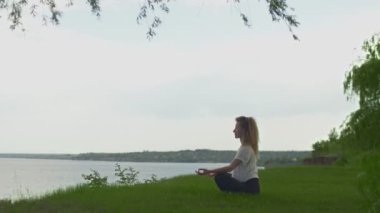 Göl ya da denizin kıyısında yoga yapan genç ve formda bir kadının yan görüntüsü. Lotus poz verip meditasyon yapan bir kadın.